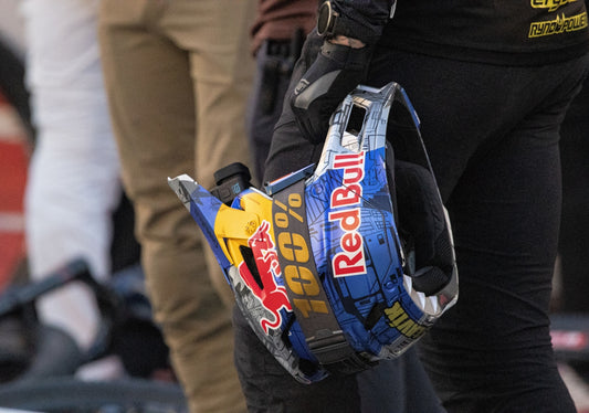 Rider holds red bull branded helmet with 100% logo.